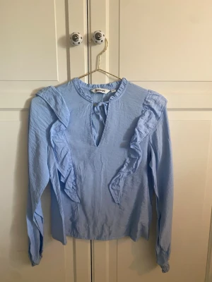 Ljusblå volangblus från Kappahl  - Supersöt ljusblå blus med volangdetaljer framtill och längs axlarna. Blusen har lång ärm, rund halsringning med liten knytning💕💕