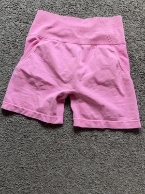 Rosa högmidjade shorts från Peach - Säljer ett par ljusrosa högmidjade shorts från Peach. De är tillverkade i ett stretchigt material med bred ribbad midja för extra komfort. Perfekta för träning eller chill dagar. Snygg och enkel design utan fickor eller synliga detaljer.