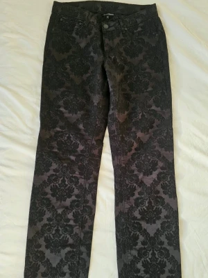 🖤 Vintage Gotiska Byxor stl.M, Jacquard / Damast (Oanvända!) 🖤 - Helt oanvända svarta vintagebyxor i en fantastisk gotisk stil! 💀 De har ett djupt, vackert mönster i jacquard-/damaststil.Obs! Tyget är helt svart i verkligheten. Detaljbilderna har ljusats upp något av kameran för att mönstret ska synas tydligare. Märkta storlek 38 och  något lägre midjan. ✨🥀 Skick: Aldrig använda 🖤📐 Exakta mått (mätta platt)Midja: 39 × 2 cm  Midjehöjd: 22 cm  Innerbenslängd: 80 cm  Benöppning: 15 × 2 cm