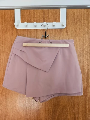 Rosa skort - Skort med dekorativ front och fake-fickor baktill. Dragkedja finns i sidan.