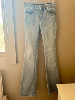Ljusblå bootcut jeans - Säljer ett par ljusblå bootcut jeans med klassisk femficksmodell och hög midja. Jeansen har en lätt tvättad look och vida ben från knät och ner. Perfekta för dig som gillar retrostil och vill ha ett par bekväma jeans i mjukt denimtyg.