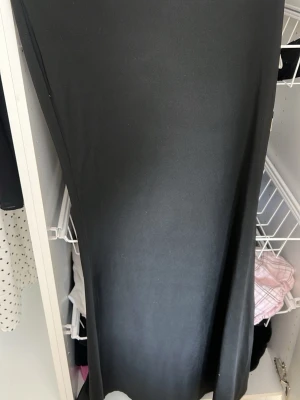 Svart långkjol i mjukt material - En stilren svart långkjol med enkel och rak passform. Kjolen har en slät yta och faller snyggt längs benen. Perfekt för dig som gillar minimalistisk stil och vill ha en kjol som funkar till många olika looks.
