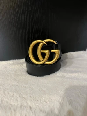 Svart Gucci läderbälte med GG-spänne - Snyggt Gucci svart bälte i läder med ett stort, guldigt GG-spänne framtill. Perfekt accessoar för att lyfta vilken outfit som helst och ger en lyxig känsla. Bältet har en klassisk design och passar till både jeans och byxor.