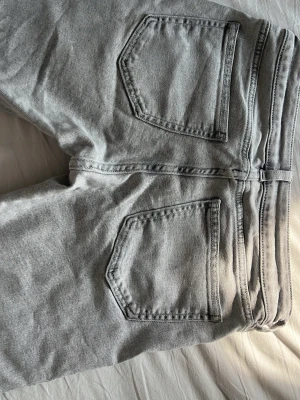 Grå raka jeans med stora bakfickor - Snygga grå jeans med raka ben och två stora bakfickor. Jeansen har klassisk femficksdesign och är tillverkade i ett mjukt denimtyg. Perfekta för en avslappnad och trendig look.