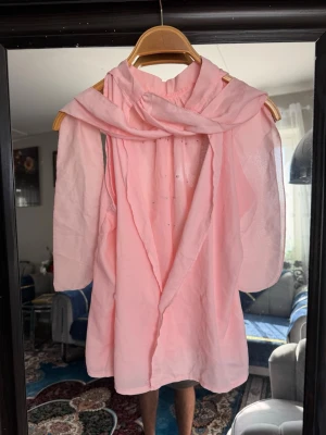Ljusrosa chiffongblus med sjal - Säljer en ljusrosa blus i tunn chiffong med långärmad design och matchande sjal. Blusen har knäppning framtill och ett luftigt, flowy fall. Perfekt för dig som gillar en feminin och elegant stil.