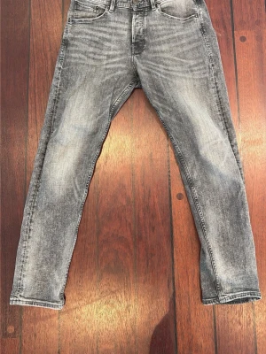 Grå tvättade slim fit jeans - Snygga grå jeans med tvättad look och smal passform. Klassisk femficksmodell med dragkedja och knapp i midjan. Jeansen har en modern, något sliten finish och raka ben. Perfekta till en avslappnad streetstil.