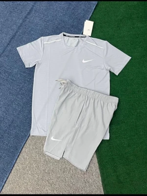 Ljusgrått träningsset från Nike - Säljer ett ljusgrått träningsset från Nike med t-shirt och shorts. Setet har en sportig design med vita Nike-loggor på både tröjan och shortsen. Tillverkat i ett lätt och snabbtorkande material som passar perfekt för träning eller gym.