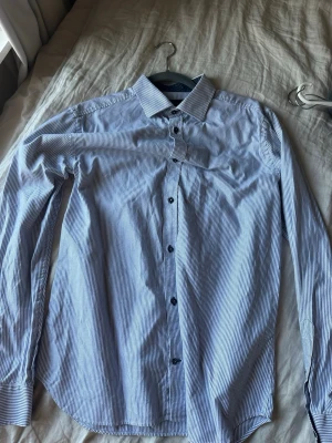 Blårandig skjorta från Riley - Snygg blårandig skjorta från Riley med klassisk krage och knappar framtill. Skjortan har lång ärm och är tillverkad i bomull. Perfekt för en stilren look.