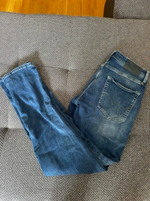Blå jeans från Jack & Jones - Snygga blå jeans från Jack & Jones med klassisk femficksmodell och gulddetaljer vid knapparna. Jeansen har en tvättad look och raka ben. Perfekta för dig som gillar en avslappnad men stilren stil.( pris kan diskuteras vid snabb affär)