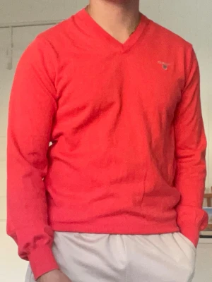 Röd V-ringad tröja från Gant - Snygg röd V-ringad tröja från Gant med diskret logga på bröstet. Tröjan har långa ärmar och ribbade muddar vid ärmslut och nederkant. Perfekt för en stilren och avslappnad look.