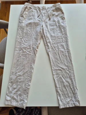 Beiga linnebyxor med dragsko - Snygga och luftiga linnebyxor i beige med raka ben och elastisk midja med dragsko. Byxorna har sidofickor och är perfekta för en avslappnad stil. Materialet är linne som ger en skön och sval känsla.