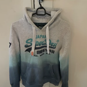 Superdry hoodie  - Säljer en snygg vintage Superdry hoodie i storlek M, modellen är ca 178. Skulle säga att tröjan passar någon som är runt 178 men helst under. Priset ej hugget sten🪨🪨  textens färg har börjat färga av sig så man måste tvätta den.