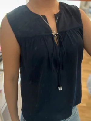 Mörkblå ärmlös blus från STOCKH LM - Snygg mörkblå blus från STOCKH LM i ärmlös modell. Toppen har en v-ringning med knytband framtill som ger en avslappnad men chic look.