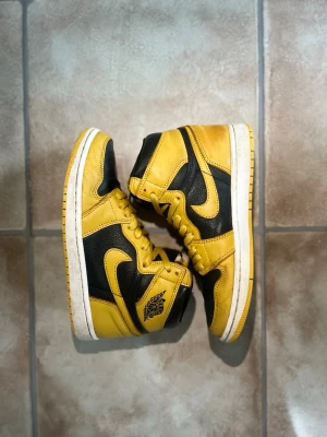 Nike Air Jordan 1 High ”Pollen” – Stl 40  - Säljer ett par schyssta Nike Air Jordan 1 High i färgkombinationen ”Pollen” (gul och svart) i storlek 40. De är använda men har väldigt mycket kvar att ge, och både sulan och undersidan är i riktigt bra skick med minimalt slitage. Det finns en del ytliga fläckar och märken på det gula lädret som syns på bilderna, men inget som påverkar användningen och det går säkert att snygga till ännu mer med lite skorengöring. Skriv gärna om du har några frågor eller vill ha fler bilder, jag fraktar snabbt! 