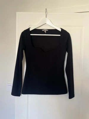 Svart långärmad topp från H&M - En svart långärmad topp från H&M med fyrkantig urringning. Toppen har en slim passform och är tillverkad i mjukt stretchigt material som sitter snyggt på kroppen. Perfekt att styla med jeans eller kjol för en clean look.