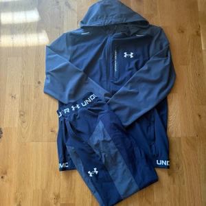 Under Armour träningsset marinblå - Snyggt träningsset från Under Armour i marinblått. Setet består av en hoodie med dragkedja och ficka på bröstet samt matchande tights med logga och elastisk midja. Perfekt för gymmet eller löprundan. Materialet är stretchigt och andas bra. Aldrig använd typ‼️‼️