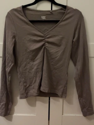 Beige långärmad topp med rynk - Säljer en beige långärmad topp från 157 med v-ringning och snygg rynkdetalj framtill. Tillverkad i mjukt och stretchigt material som sitter skönt på kroppen. Perfekt att matcha med jeans eller kjol för en enkel och clean look.