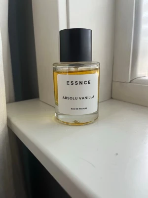 ESSNCE Absolu Vanilla parfym - Upptäck ESSNCE Absolu Vanilla Eau de Parfum i en stilren, rund glasflaska med svart lock. Doften har en varm, vaniljig ton och flaskan har en minimalistisk vit etikett. Perfekt för dig som gillar söta och mjuka dofter. Inspirerad av ”kayali vanilla 28”. Använd att fåtal gånger.