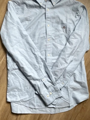 Ljusblå oxfordskjorta Regular Fit - Klassisk ljusblå oxfordskjorta i Regular Fit köpt från Gant. Har endast testat skjortan annars har den bara legat, storleken är M.                                 Nypris är ca 1199kr, säljs för 700 (pris är ej hugget i sten, kom gärna med bud!)