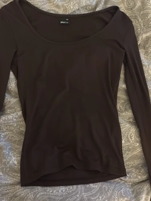 Brun långärmad topp från Gina Tricot - Mörkbrun långärmad topp från Gina Tricot med rund, bred urringning. Tillverkad i ett mjukt och stretchigt material som sitter tight mot kroppen. Perfekt att styla med jeans eller kjol för en clean look.