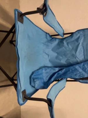 Blå hopfällbar campingstol - Praktisk blå hopfällbar campingstol med armstöd och svart metallstomme. Perfekt att ta med till stranden, festivalen eller utflykten. Stolen är lätt att fälla ihop och bära med sig tack vare sin smidiga design.