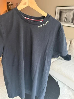 Mörkblå Hilfiger t-shirt - Snygg mörkblå t-shirt från Hilfiger med diskret logga vid halsen. Klassisk rund halsringning och korta ärmar. Tillverkad i mjuk bomull som känns skön mot huden. Perfekt till jeans eller shorts för en clean look.