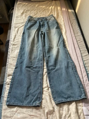 Blåa wide leg jeans med hög midja - Säljer ett par blåa jeans med breda ben och hög midja. Jeansen har klassisk femficksdesign och är tillverkade i denim med en lätt tvättad look. Perfekta för en avslappnad och trendig stil.