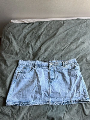 Ljusblå jeanskjol med fickor - Trendig ljusblå jeanskjol i kort modell med klassiska fickor fram och knappstängning. Perfekt till vardags för en avslappnad och cool stil. Passar snyggt med både sneakers och boots.