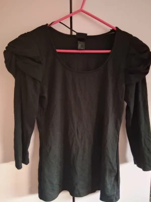 Svart topp med puffärmar - Stilren svart topp med långa puffärmar och rund halsringning. Toppen har en figurnära passform och är tillverkad i mjukt bomullsmaterial. Perfekt för dig som vill ha en enkel men trendig look.