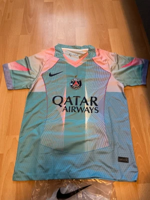 PSG matchtröja i pastellfärger - Säljer en PSG matchtröja från Nike i pastellfärger med inslag av ljusblått, rosa och lila. Tröjan har korta ärmar, V-ringning och tryck med Qatar Airways på bröstet samt PSG-logga. Tillverkad i lätt och ventilerande funktionsmaterial.