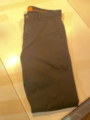Mörkgrå chinos från Hugo Boss - Snygga mörkgrå chinos från Hugo Boss med klassisk rak passform och diskreta sidofickor. Tillverkade i ett mjukt bomullsmaterial som ger en skön känsla och stilren look. Perfekta för dig som vill ha en clean och modern stil.