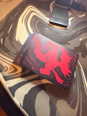 Pokémon astral raidience hållare  samlarkort - Unikt Pokémon samlarkort med astral raidience i röd och svart design. Kortet har en stiliserad illustration med skarpa linjer och kontrasterande färger, perfekt för dig som gillar att samla eller spela Pokémon TCG. Materialet är klassiskt glansigt papp.