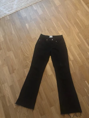 Svarta lågmidjade bootcut jeans från Abrand - Säljer ett par svarta bootcut jeans från Arket med råa kanter nertill. Jeansen har klassisk femficksdesign, hög midja och knappgylf. Perfekta för dig som gillar en tidlös men trendig look.