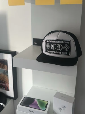 Chrome hearts keps - Säljer en Chrome Hearts Trucker Cap i färgställningen svart, vit och silvergrå. Kepsen har det ikoniska, broderade Hollywood-patchet på framsidan samt den klassiska silverknappen på toppen. 