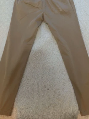 Beige chinos från MNG Man - Snygga beige chinos från MNG Man i storlek 40. Klassisk rak passform med knapp- och dragkedjegylf samt bälteshällor. Insidan har ett mönstrat tyg som ger en extra detalj. Perfekta för dig som vill ha en clean och stilren look.