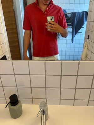 Röd pikétröja från Yves Saint Laurent - Säljer en klassisk röd pikétröja från Yves Saint Laurent med korta ärmar och krage med knappar. Tröjan har en liten broderad logga på bröstet och är gjord i mjuk bomull. Perfekt för dig som vill ha en stilren och tidlös topp.