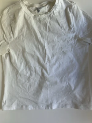 Klassisk vit t-shirt i bomull - En enkel och stilren vit t-shirt med rund hals och korta ärmar. Perfekt basplagg som passar till allt och är tillverkad i mjuk bomull för skön känsla hela dagen.