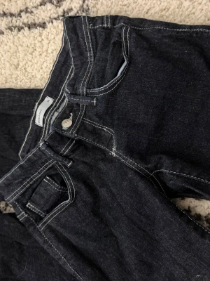 Mörkblå jeans med kontrastsömmar - Säljer ett par mörkblå jeans från Gina med vita kontrastsömmar och klassisk femficksmodell. Jeansen har normal midja och raka ben. Materialet är kraftig denim som ger en tidlös look. Perfekta för dig som gillar enkel och stilren design. (Skriv för fler bilder💕)