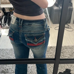 Blå lågmidjade jeans från Urban Crush - Säljer ett par as snygga blå jeans från Urban Crush med jätte coola bakfickor. Jeansen har raka ben med en liten slits längst ner på benen och klassisk femficksdesign. Märkespatch bak i midjan och dekorativa sömmar. De är köpta i Norge och har inte sett någon som har liknande. De står ingen storlek men passar mig som har typ xs! De är använda fåtal gånger men ser helt nya ut.