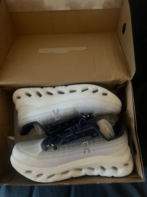 On cloud skor  - Snygga sneakers från On Running med vit och blåmesh-överdel, mörkblå detaljer och tjock, innovativ sula med hål för extra komfort. Skorna har en sportig design och är perfekta för dig som gillar att sticka ut med stilrena och moderna sneakers.