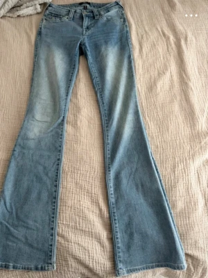 True Religion ljusblå bootcut jeans - Ljusblå jeans från True Religion, modell BECCA Mid Rise Bootcut. Jeansen har klassisk femficksdesign, bälteshällor och lätt utsvängda ben. Tillverkade i mjuk denim med snygga slitningar och tvättade detaljer för en trendig look.