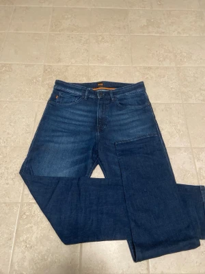 Mörkblå jeans från Hugo boss  - Snygga mörkblå jeans från Hugo Boss med klassisk femficksmodell och raka ben. Jeansen har en diskret tvättad look och är tillverkade i mjukt denimtyg med bälteshällor och knappgylf. Perfekta för en avslappnad och trendig stil. Dom är aldrig använda! Skriv för fler frågor o pris kan diskuteras 