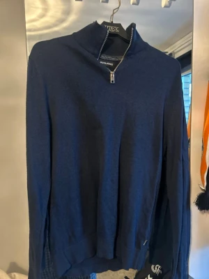 Mörkblå halvzip från Jack & Jones - Mörkblå tröja från Jack & Jones med halv dragkedja och hög krage. Tröjan har lång ärm och ribbade muddar vid ärmslut och nederkant. Perfekt för lager på lager och enkel att matcha med jeans eller chinos.