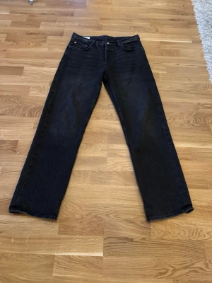 Svarta raka jeans med rå kant - Säljer ett par svarta jeans med rak passform och rå, ofållad kant nertill. Jeansen har klassisk femficksdesign och knappgylf. Perfekta för en avslappnad och trendig stil.