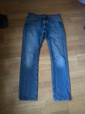 Levis 501 Jeans - Klassiska blå jeans från Levi's med rak passform och fem fickor. Jeansen har en tidlös look med knappgylf och tydliga sömmar. Perfekta för dig som gillar en enkel och clean stil. W32 L32