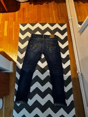 Nudie Grim Tim - Tjena! Säljer mina svinsnygga mörkblå jeans från Nudie. Dom är knappt använda och är i väldigt fint skick.  Enda små skavankerna är ett ytterst litet hål i bakfickan som kom av en slitning samt en liten tråd som sticker ut. Jeansen har en rak passform och är tillverkade i denim med snygg slitning på baksidan. Perfekta för en avslappnad och stilren look. Modell: Grim Tim.  Storlek: W29 L30 jag är 174 och de sitter som en smäck! Funderingar? Tveka inte på att höra av dig! MVH Strwwt Wst