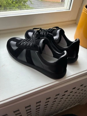 Maison Margiela Replica svarta - Jättesnygga svarta Margiela Replica sneakers. Helt oanvända. Perfekt för en snygg och stilren look i sommar.