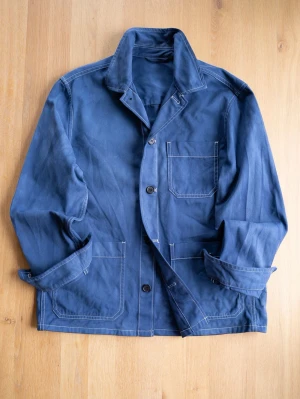 Vintage Blue Chore Jacket - Stilren blå overshirt i bomull med tre framfickor och vita kontrastsömmar. Nice patina och color bleed (se bilderna) som ger extra karaktär. Klassisk krage och knäppning med tre knappar framtill. Perfekt lager på lager-plagg för en avslappnad look.