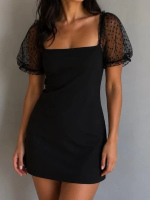 Svart kort klänning med puffärmar strl 40 - Trendig svart kort klänning med transparenta puffärmar  och små prickar på . Fyrkantig urringning och figurnära passform ger en modern look. Perfekt för dig som vill sticka ut med stilrena detaljer och coola ärmar. Helt ny men saknar pristagg 