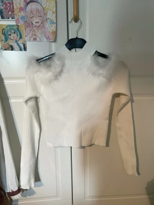 Vit stickad tröja med fuskpälsdetaljer - Trendig vit stickad tröja med långa ärmar och hög hals. Tröjan har unika fluffiga fuskpälsdetaljer på axlarna som ger en cool och lekfull look. Materialet är ribbstickat och stretchigt, perfekt för dig som vill sticka ut. Sista bilden är UNGEFÄR hur den ser ut på. Den är jätte tight bruh får inte på den. Köpt utomlands för ca 150kr. Säljer för 80. Helt oanvänd utan defekter